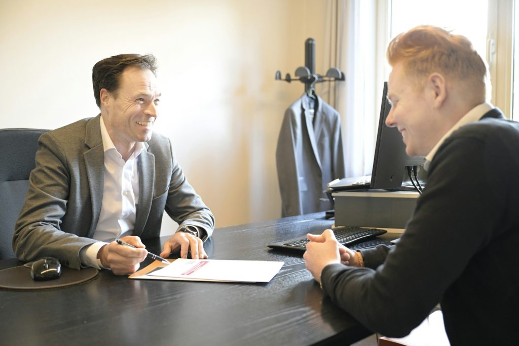 Two smiling men discussing documents at an office desk.