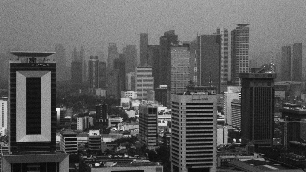 Monochromatic cityscape with tall modern buildings under a hazy sky.
